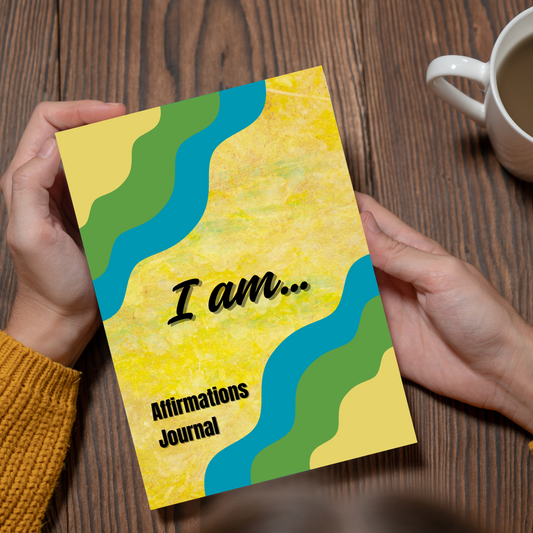 Person holding a 'I am... Affirmations Journal' with colorful design on a wooden surface.