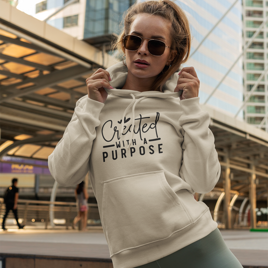 Woman wearing a beige hoodie with 'Created with a Purpose' text in an urban setting