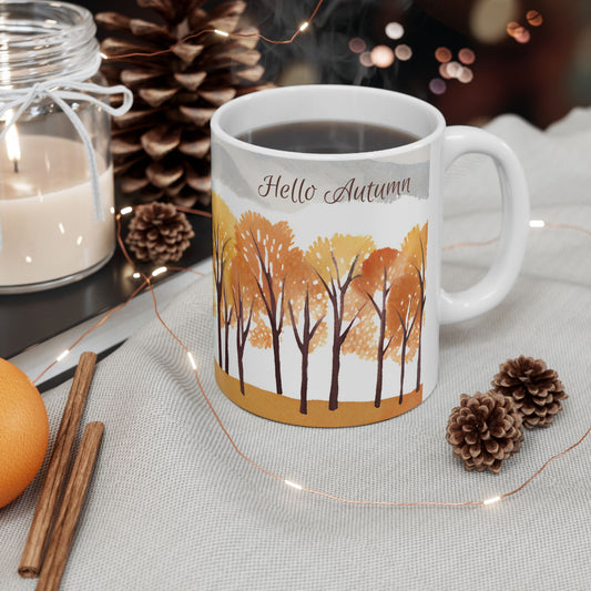 White mug with autumn design featuring trees and 'Hello Autumn' text, surrounded by decorative elements on a table.